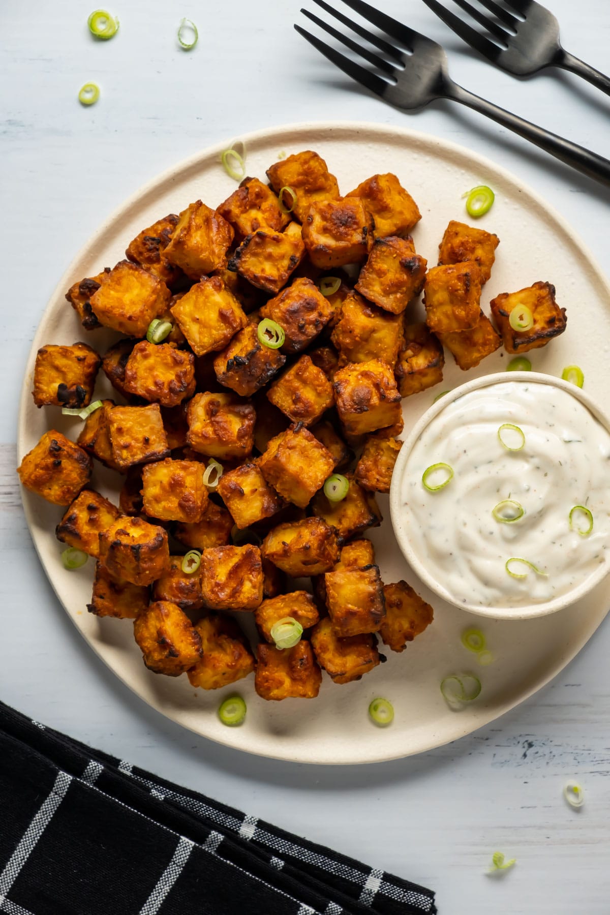 Air fryer tofu with chopped green onions on a white plate with ranch dressing. 