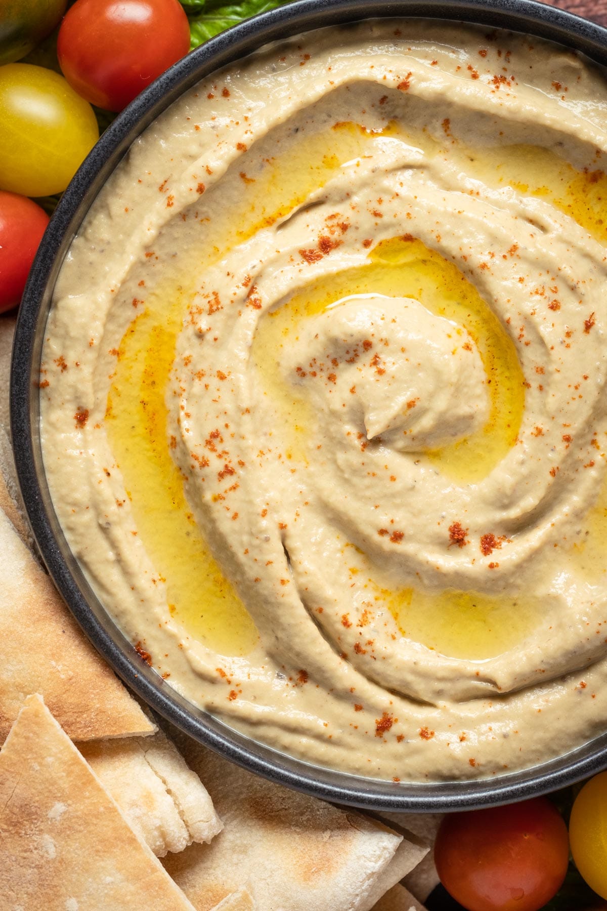 Baba ganoush in a bowl topped with smoked paprika and olive oil, with cherry tomatoes and pita breads on the side.