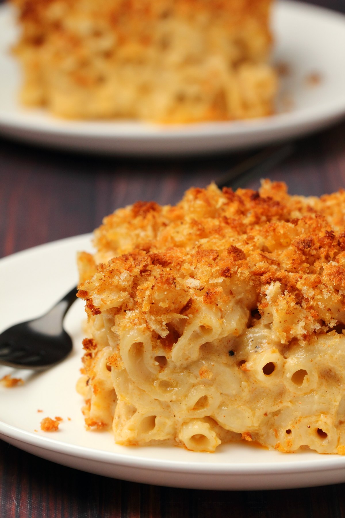 A slice of baked vegan mac and cheese on a white plate with a fork. 