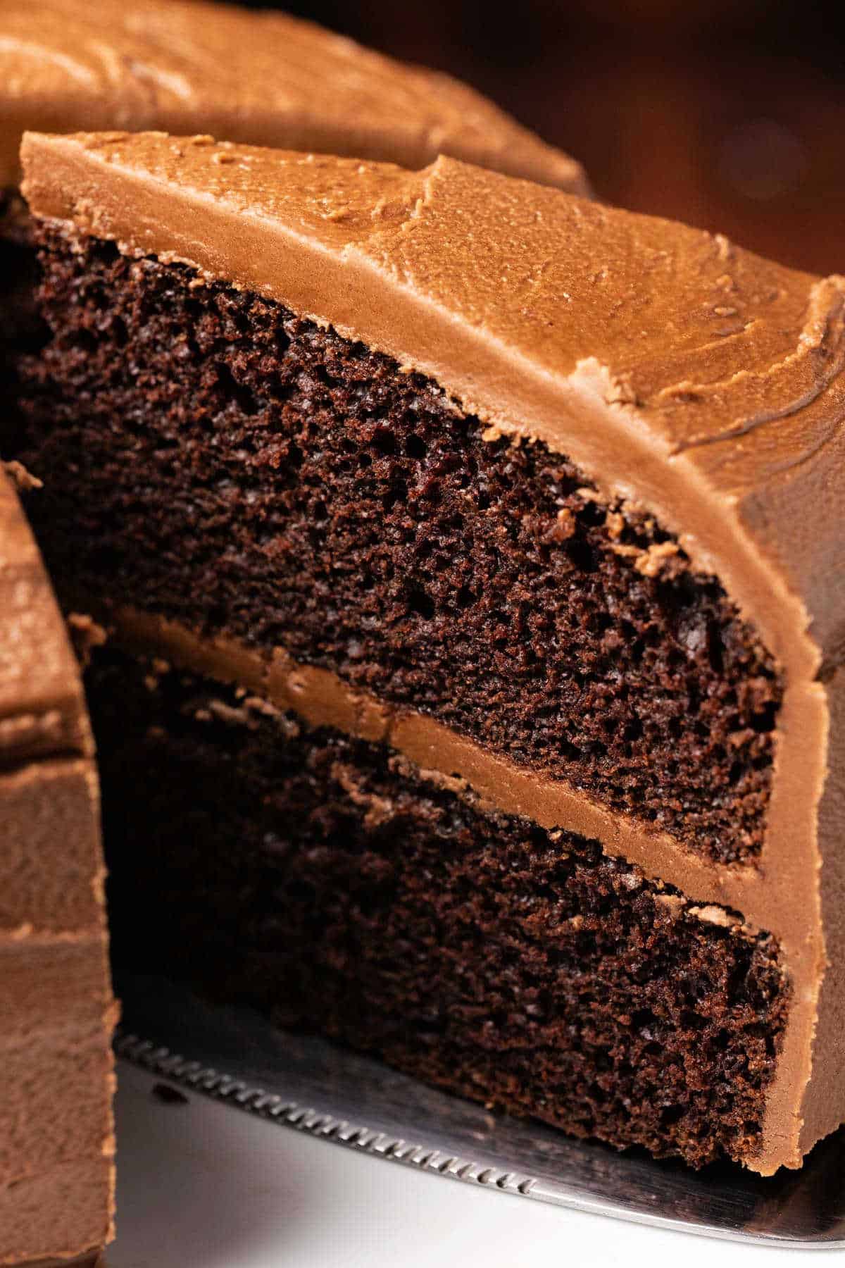 Chocolate cake on a white cake stand with one slice cut and ready to serve. 