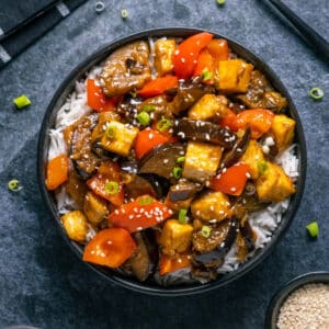 Eggplant tofu stir fry with rice in a black bowl.