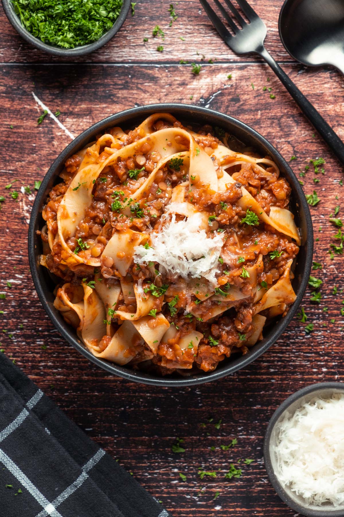 Lentil ragu with vegan parmesan and fresh chopped parsley in a black bowl.