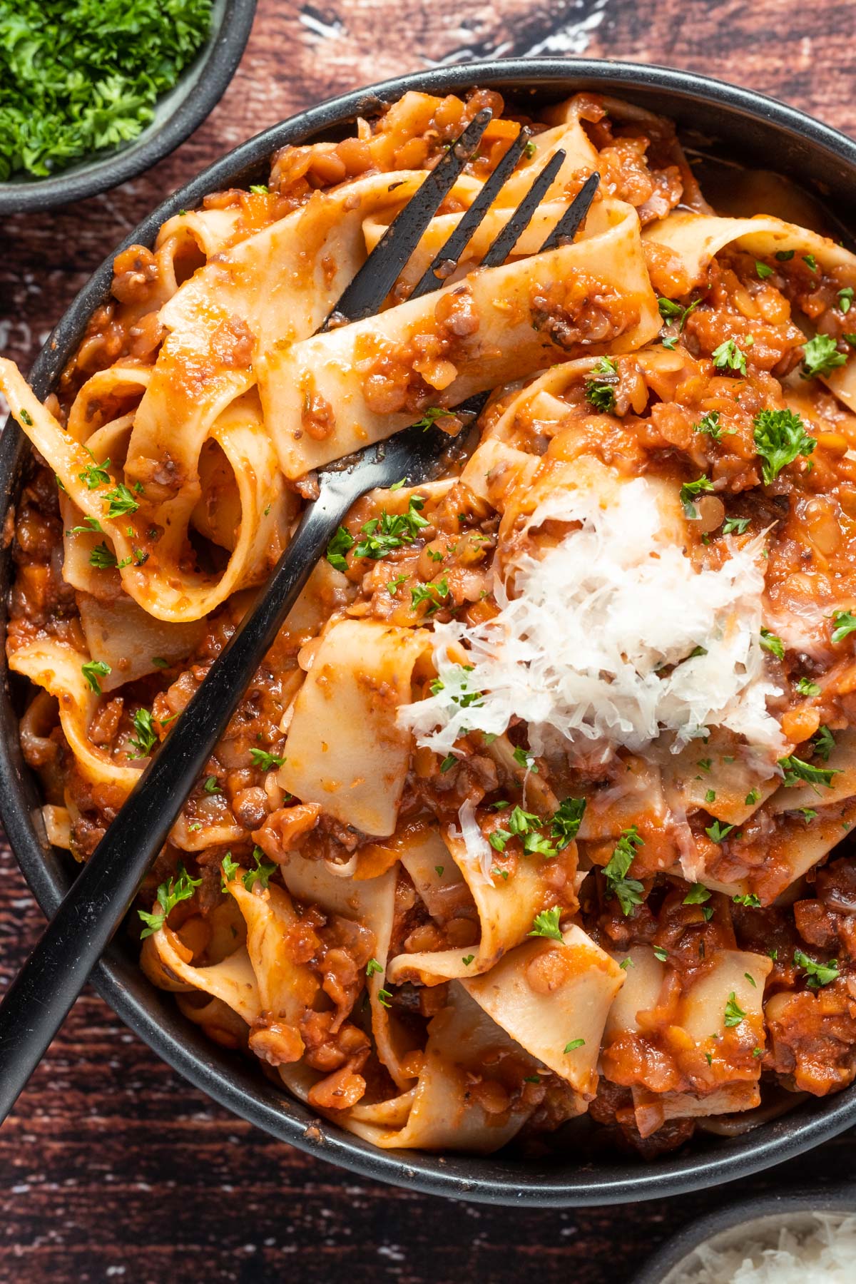 Lentil ragu with vegan parmesan and fresh chopped parsley in a black bowl with a fork.