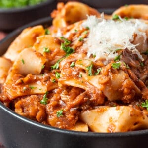 Lentil ragu with vegan parmesan and chopped parsley in a black bowl.