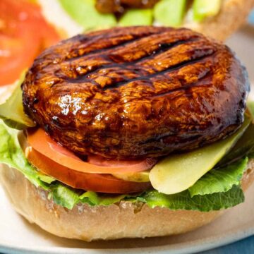 Portobello burger with lettuce, tomato, pickle on a white plate.