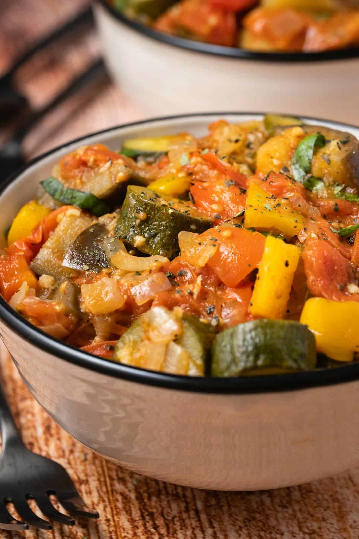 Ratatouille topped with ground black pepper and dried oregano in a ceramic bowl. 