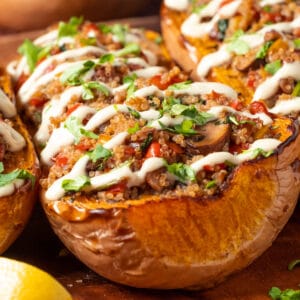 Stuffed butternut squash drizzled with cashew cream and sprinkled with fresh chopped cilantro on a serving platter.