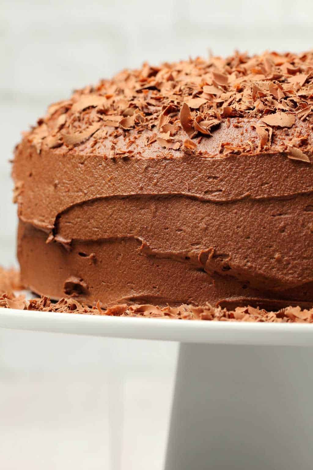 Chocolate cake topped with chocolate shavings on a white cake stand. 