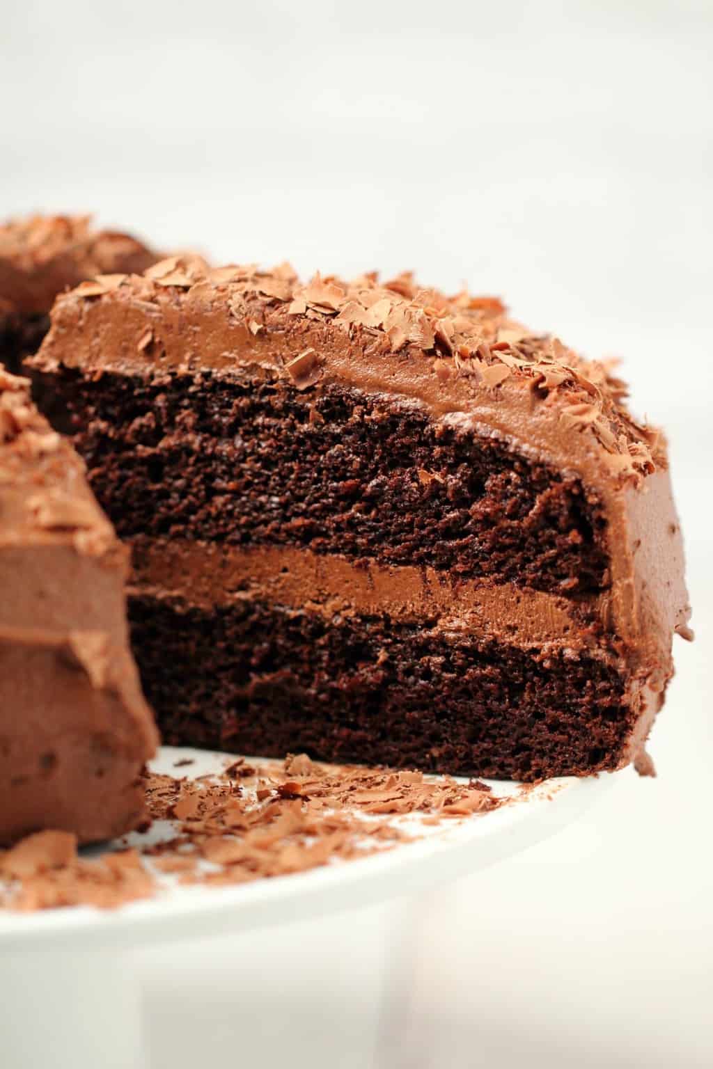 Chocolate cake on a white cake stand with one slice cut and ready to serve. 