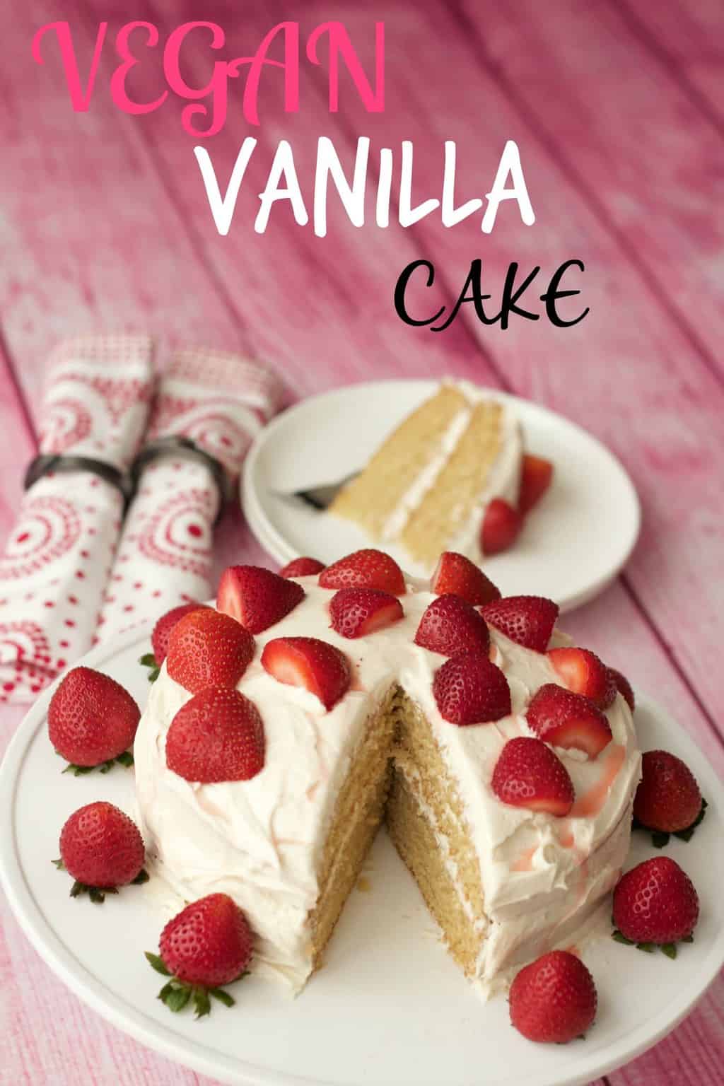 Vegan vanilla cake topped with fresh strawberries on a white cake stand. 