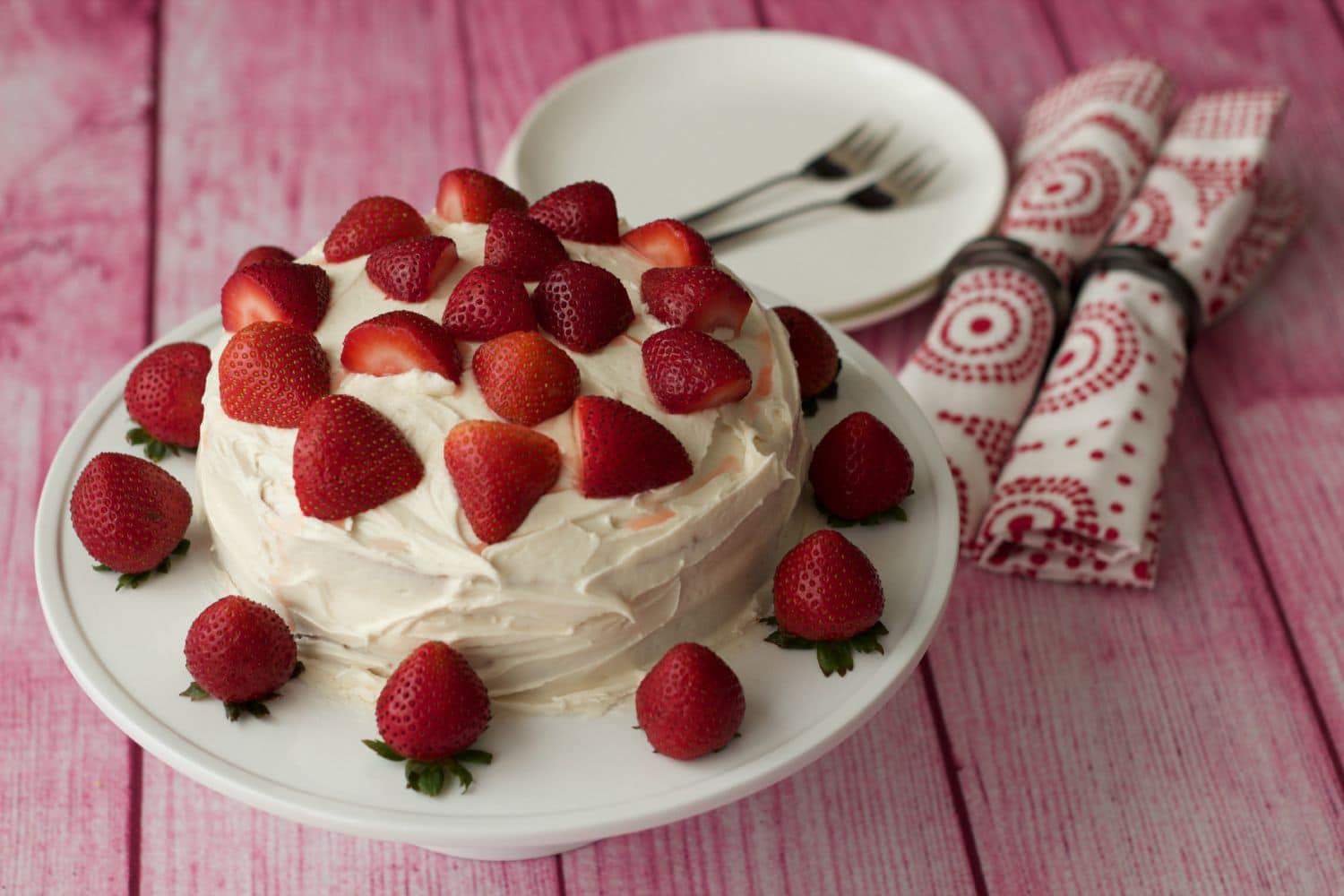 Vegan vanilla cake topped with fresh strawberries on a white cake stand. 