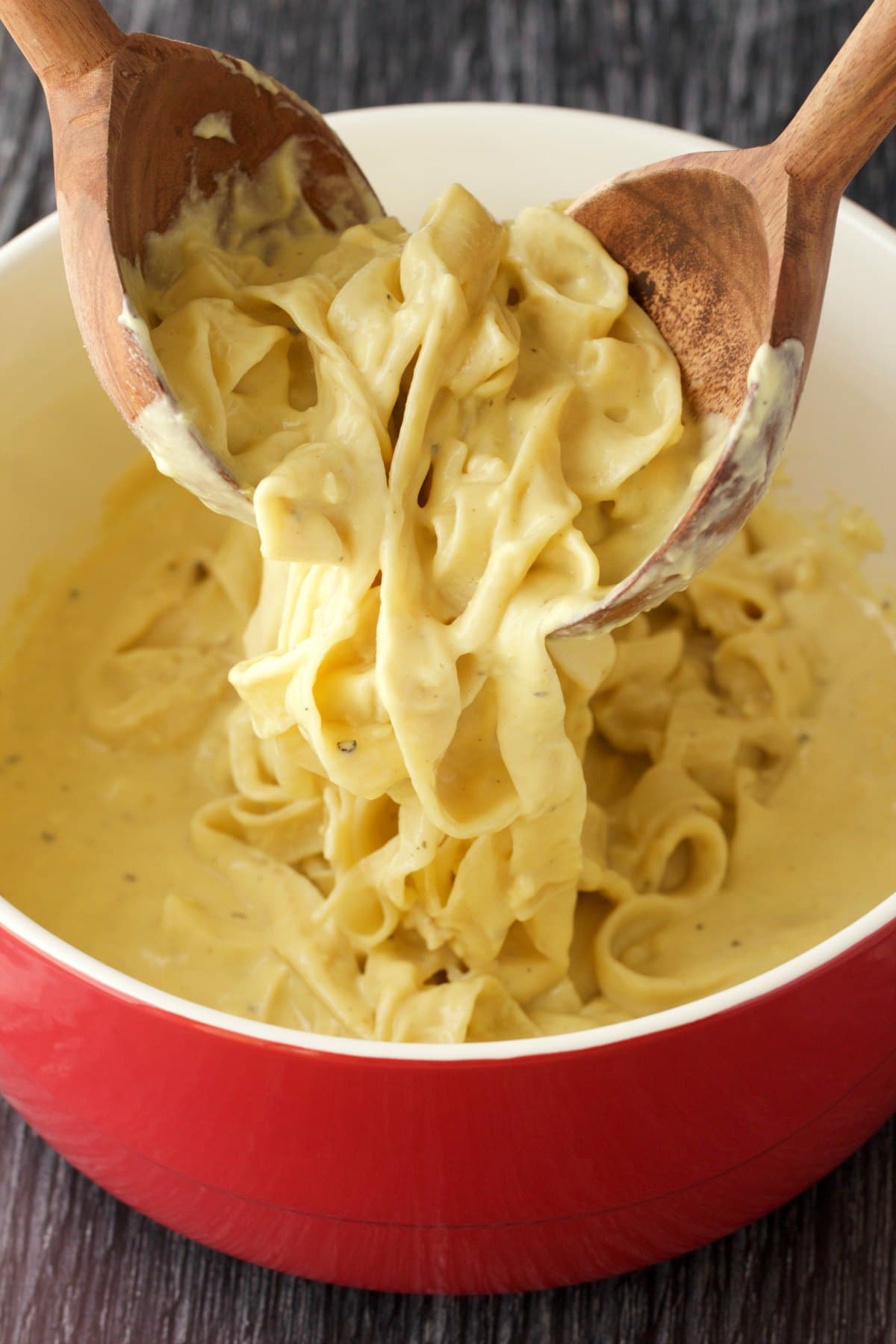 Tossing some vegan fettucine alfredo in a red and white serving dish. 