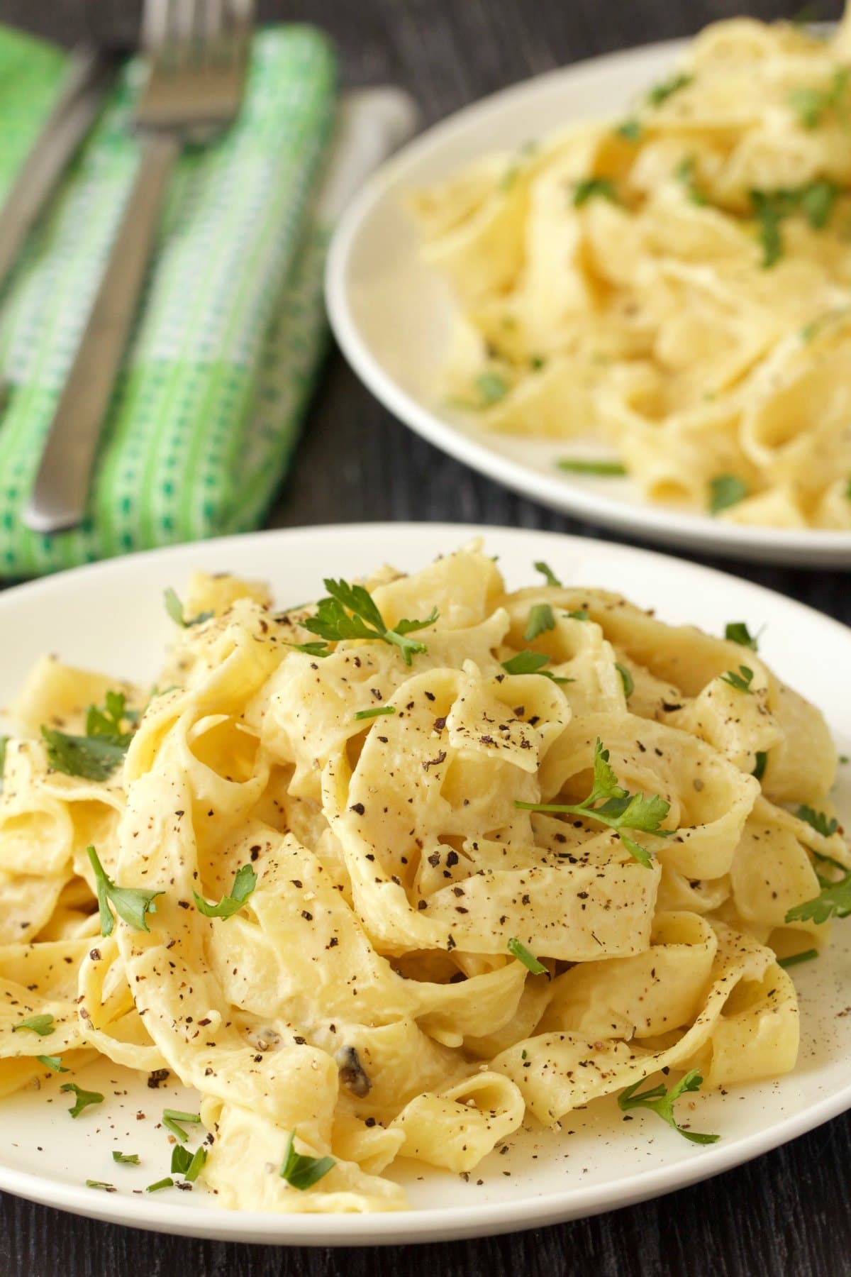 Vegan fettucine alfredo with fresh parsley and black pepper on a white plate. 