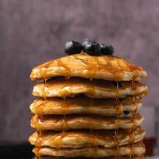 Vegan blueberry pancakes stacked up on a white plate.