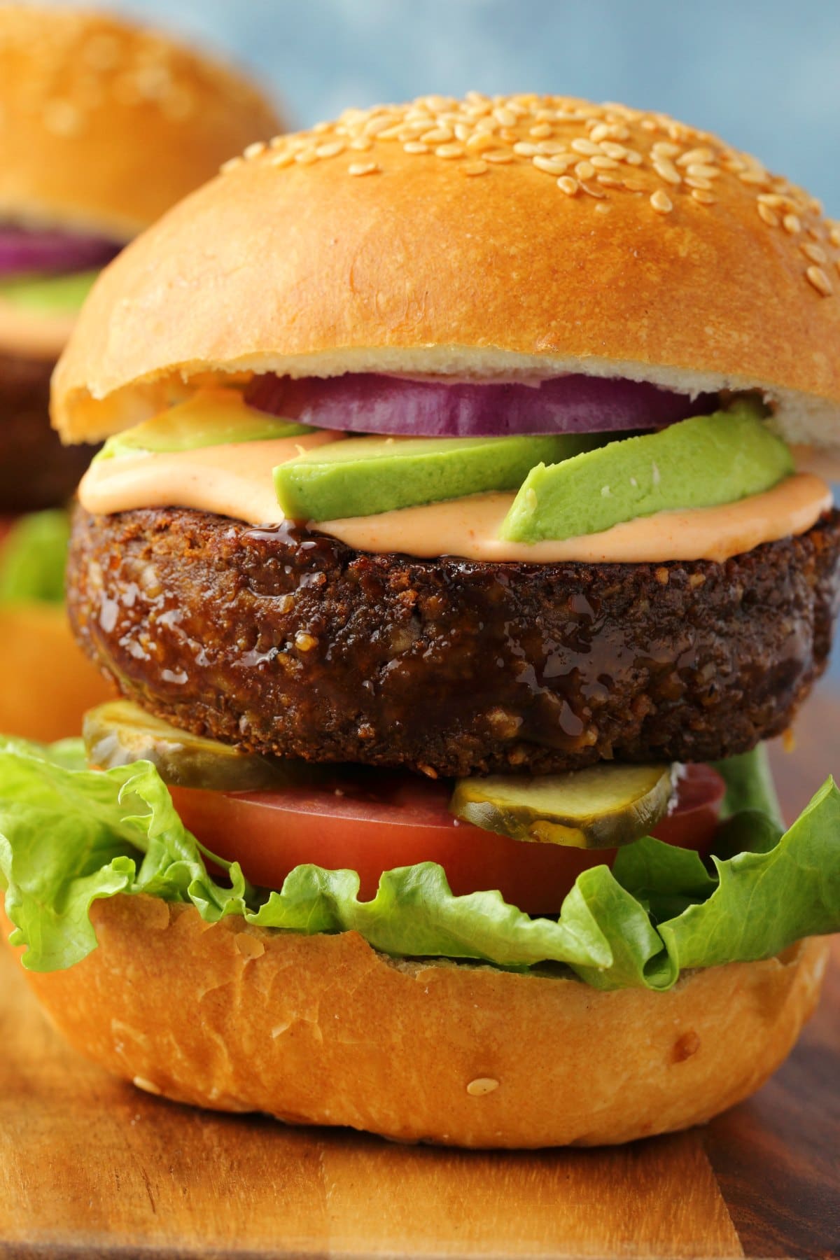 Vegan burger on a burger bun with lettuce, tomato, pickles, avocado and red onion. 