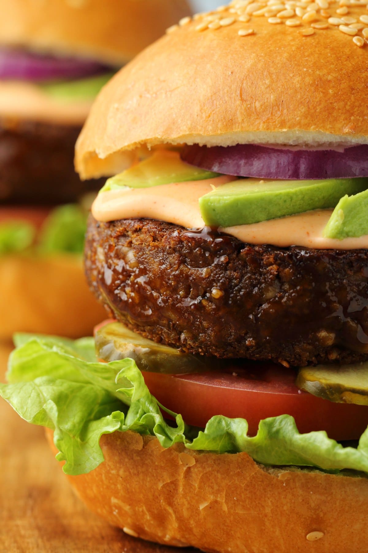 Vegan burger on a hamburger bun with lettuce, tomato, pickles, avocado, red onion and vegan thousand island dressing. 