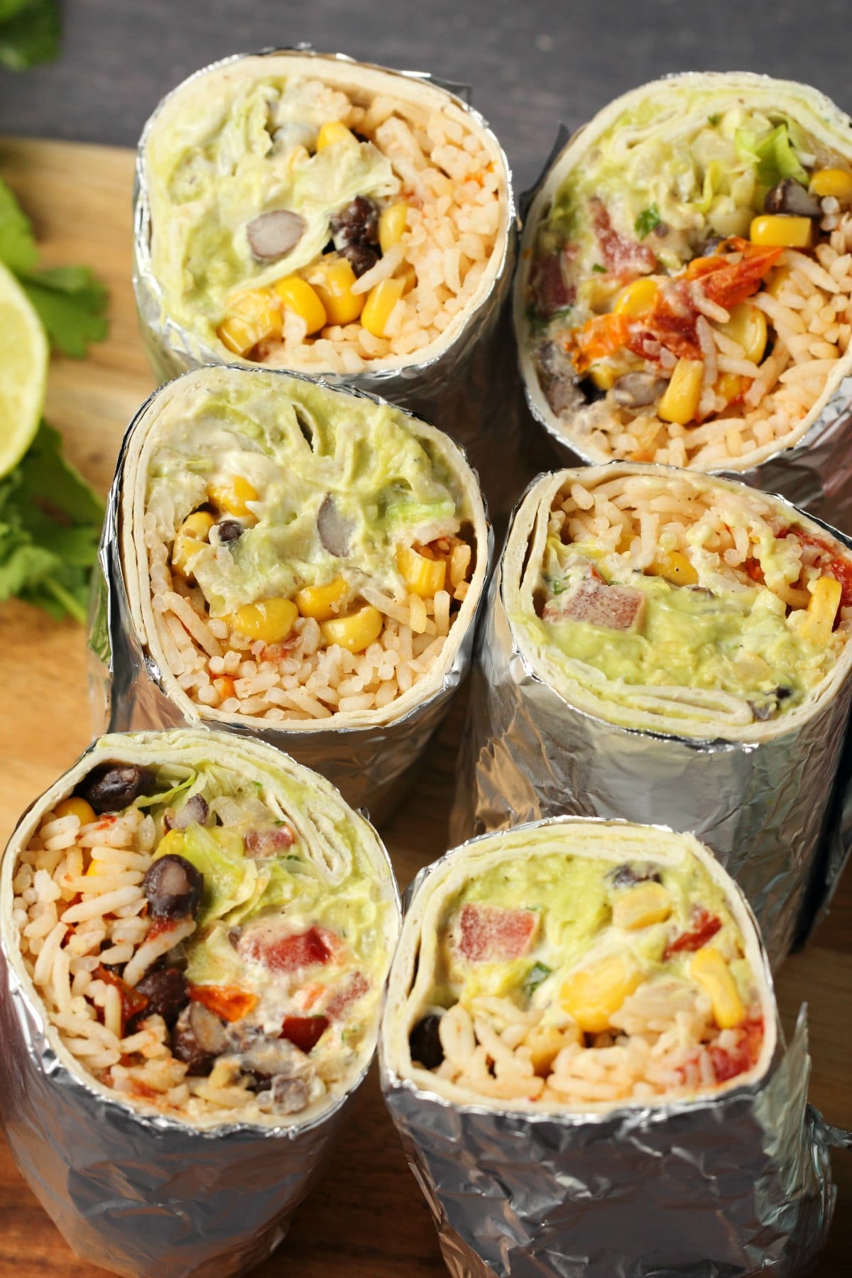 Vegan burritos cut in half and standing upright on a wooden cutting board. 