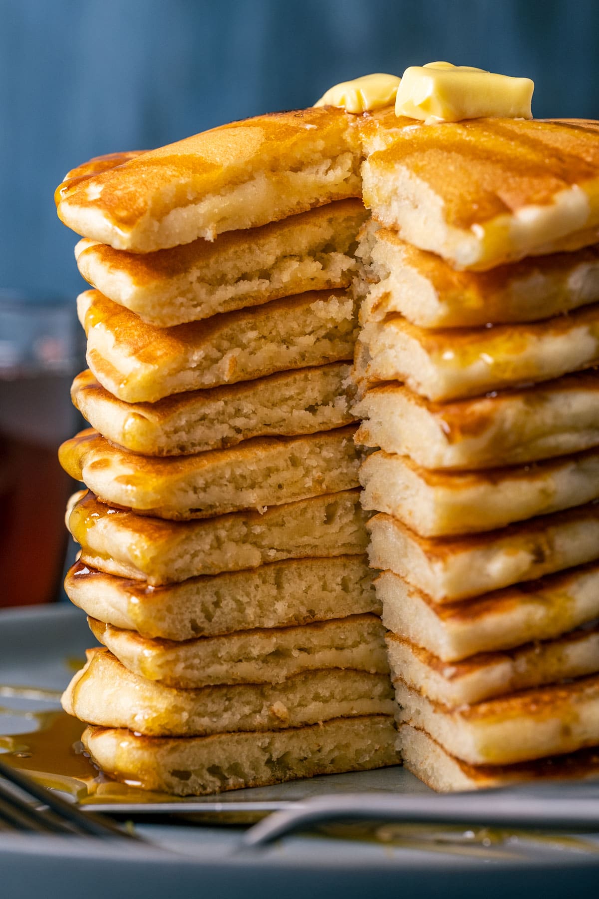 Stack of vegan buttermilk pancakes topped with vegan butter and syrup on a blue plate.