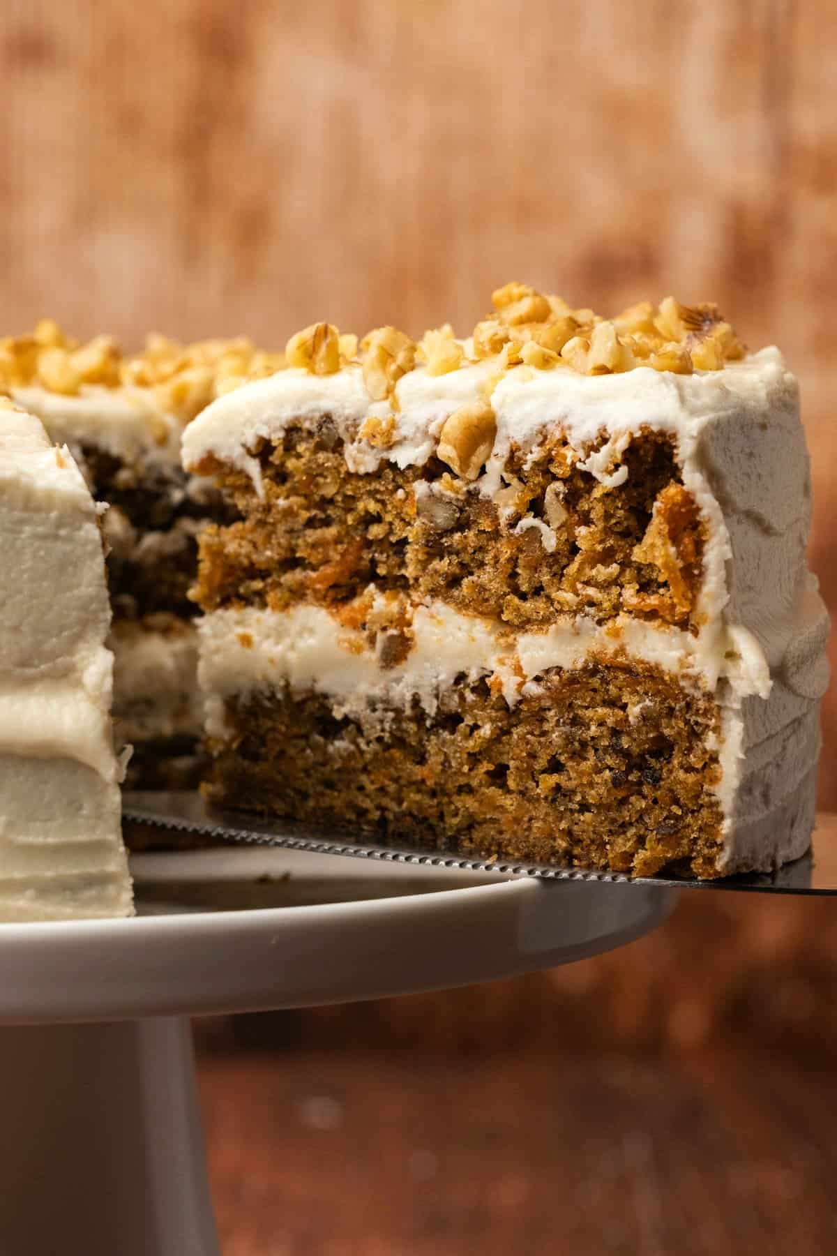 Sliced vegan carrot cake on a white cake stand. 