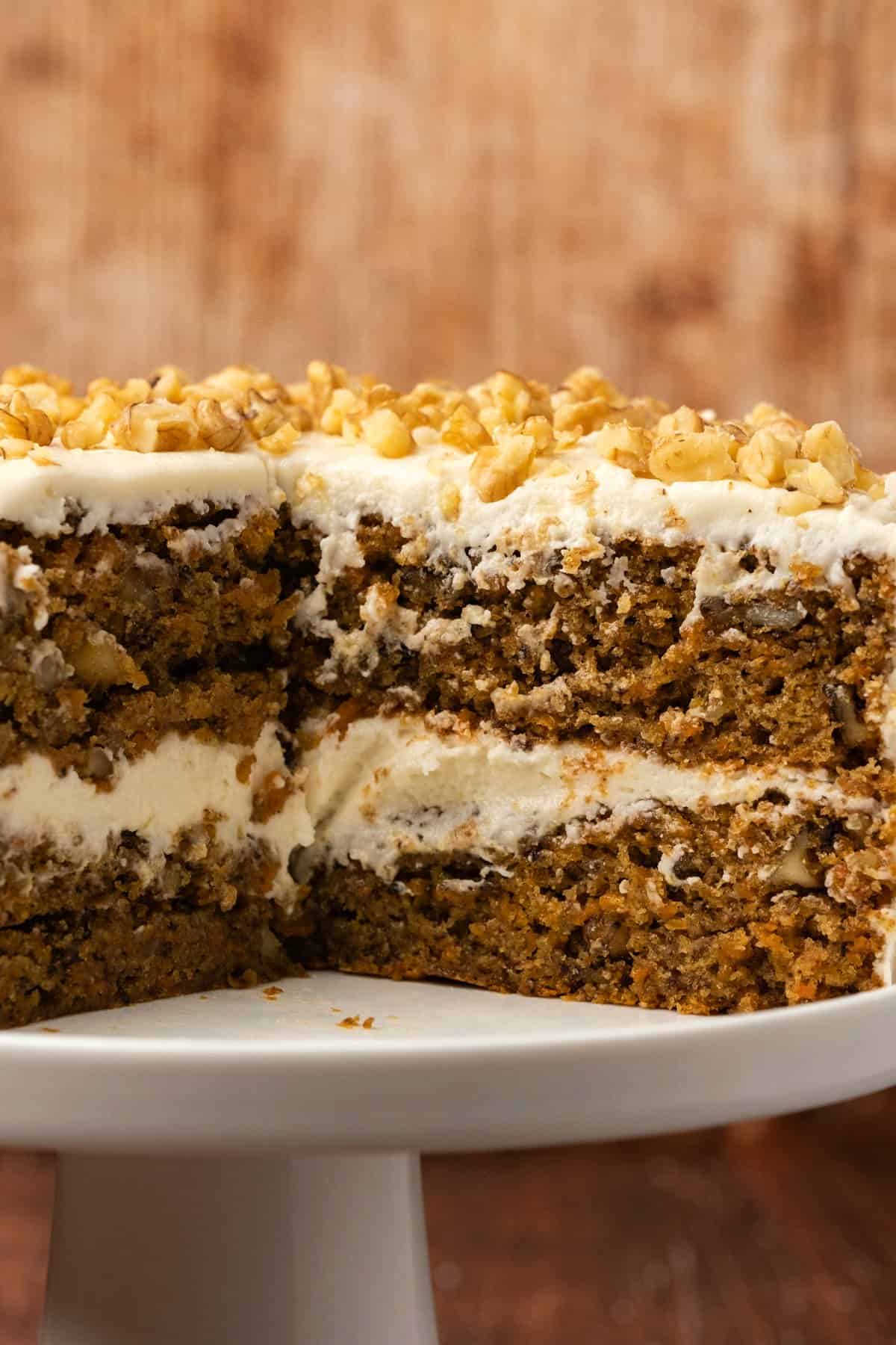 Vegan carrot cake with a few slices removed on a white cake stand.