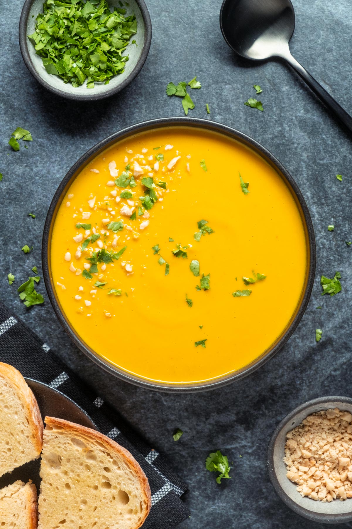 Vegan carrot soup in a black bowl with fresh chopped cilantro and crushed peanuts.