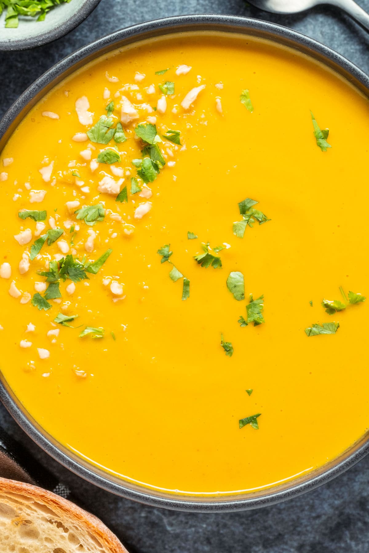 Vegan carrot soup in a black bowl with fresh chopped cilantro and crushed peanuts.