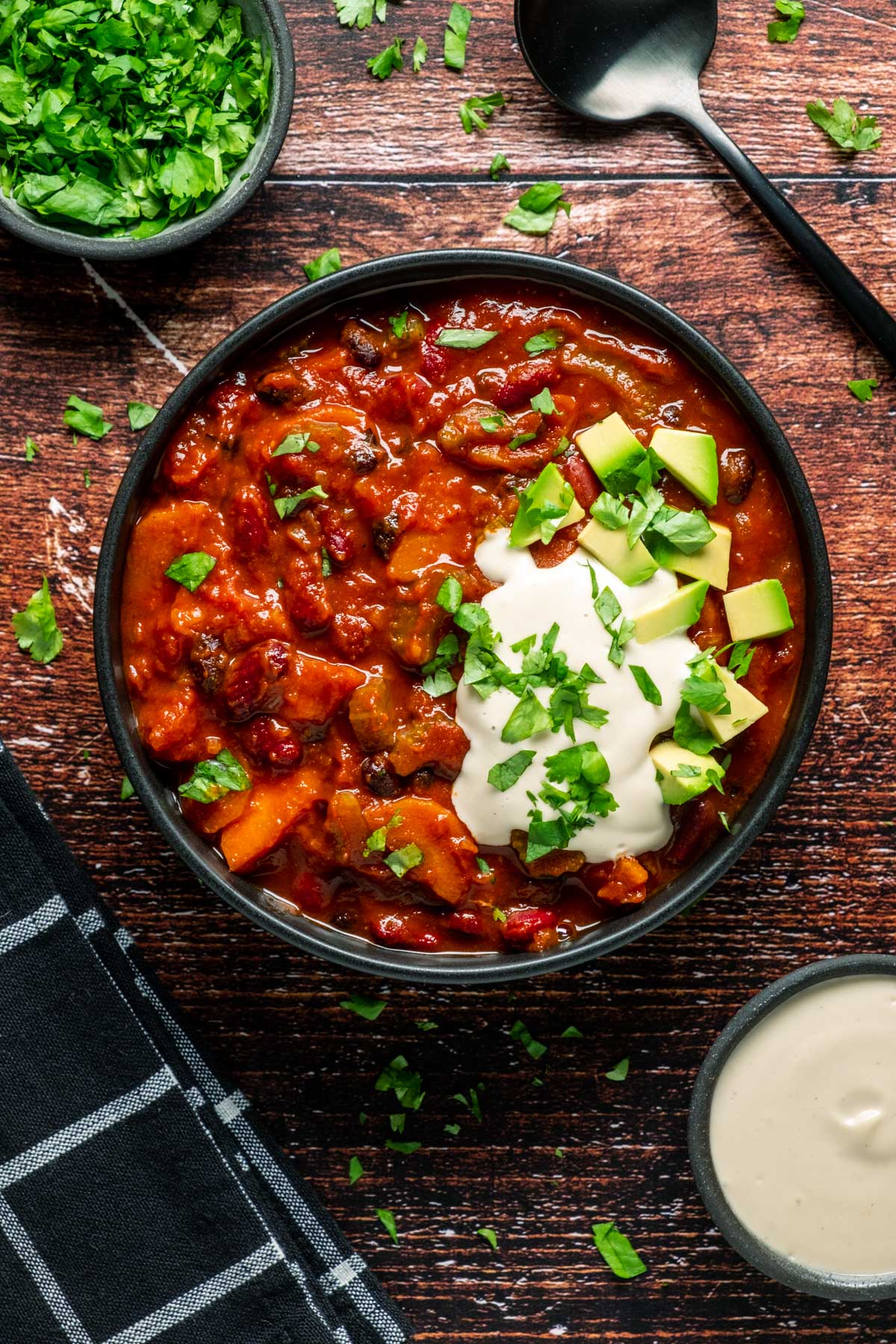 Vegan chili in a black bowl with chopped cilantro, cashew cream and diced avocado.