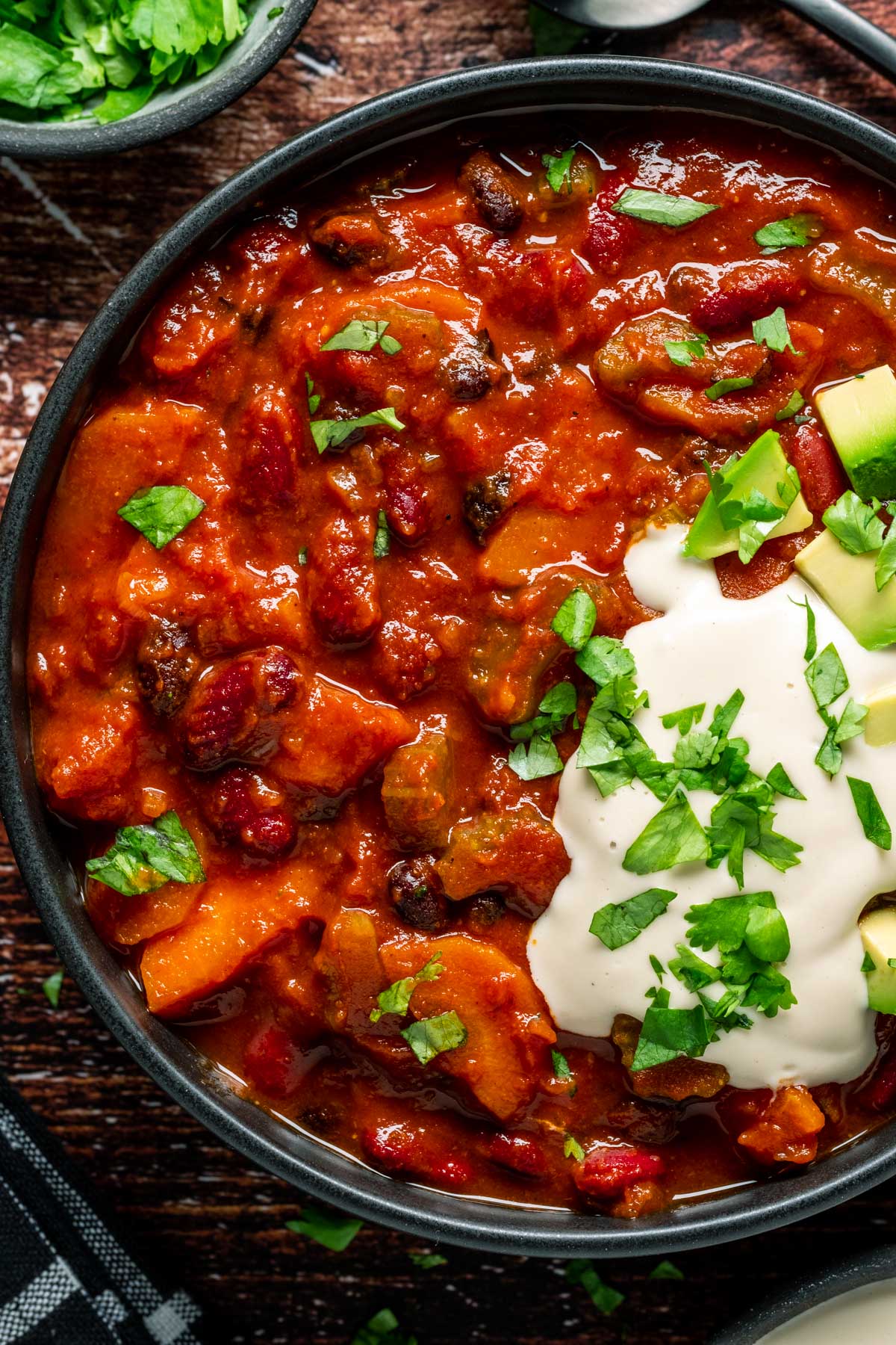 Vegan chili in a black bowl with chopped cilantro, cashew cream and diced avocado. 