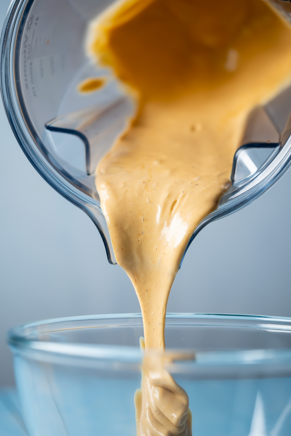 Vegan chipotle sauce pouring from a blender into a glass bowl. 