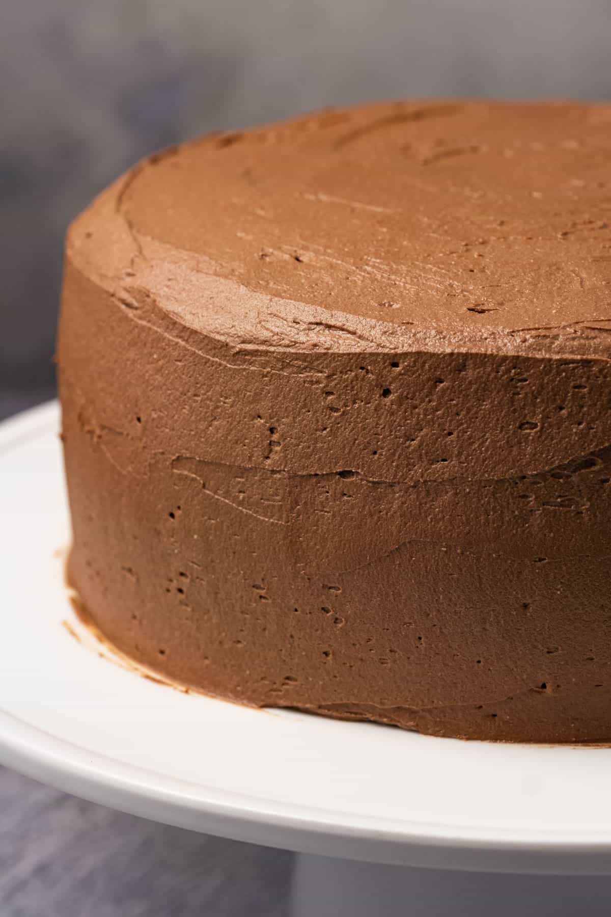 Frosted vegan chocolate cake on a white cake stand.