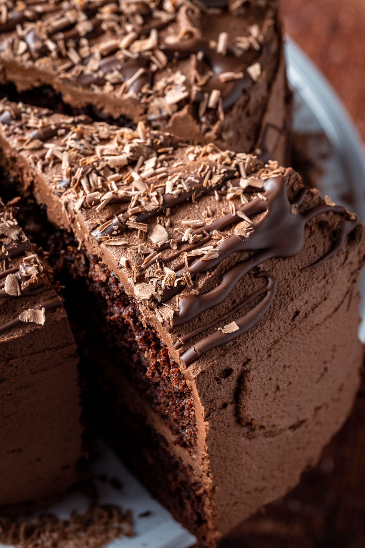 Sliced vegan chocolate fudge cake on a white cake stand.