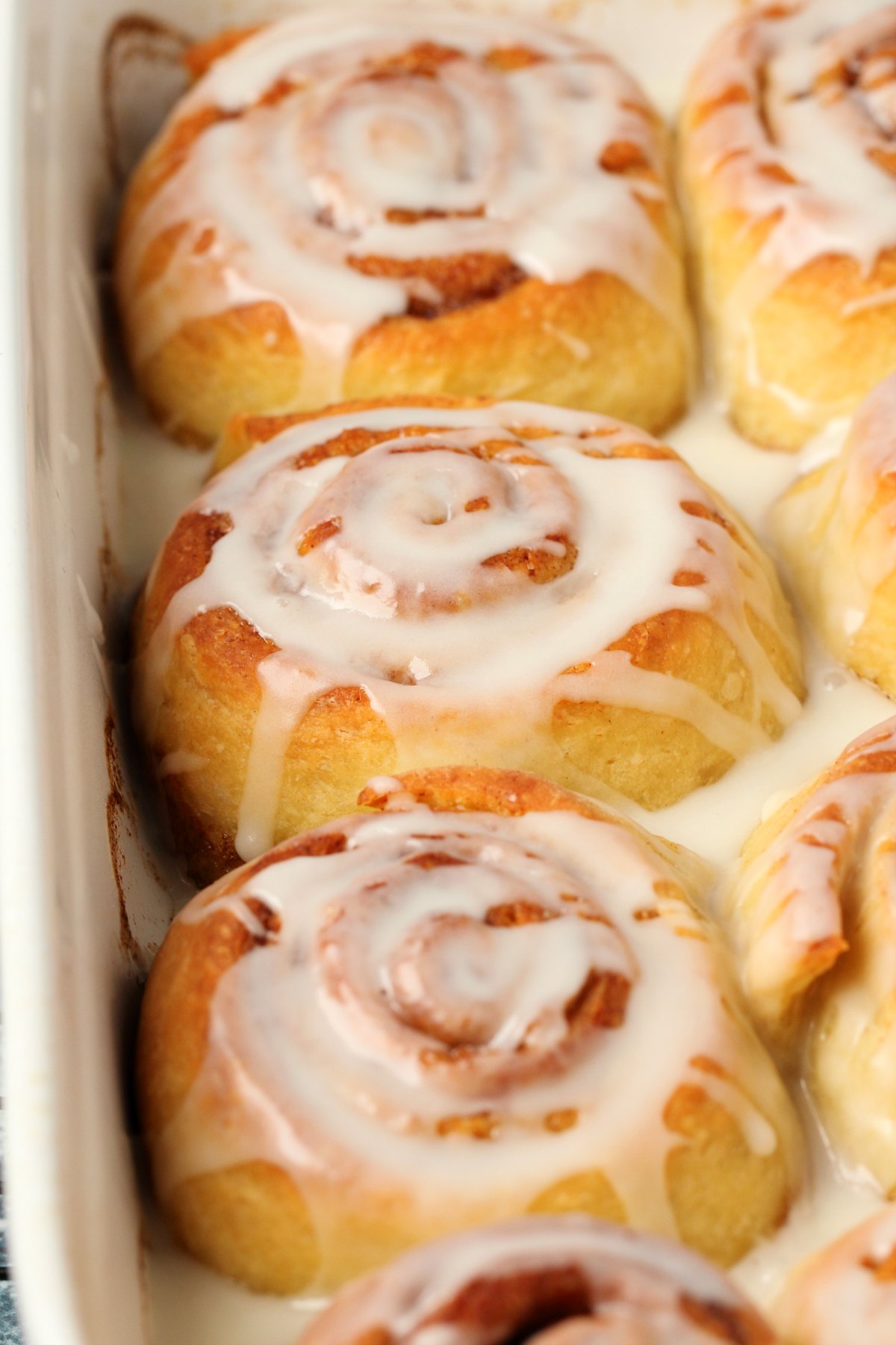 Vegan cinnamon rolls topped with frosting in a white baking dish. 