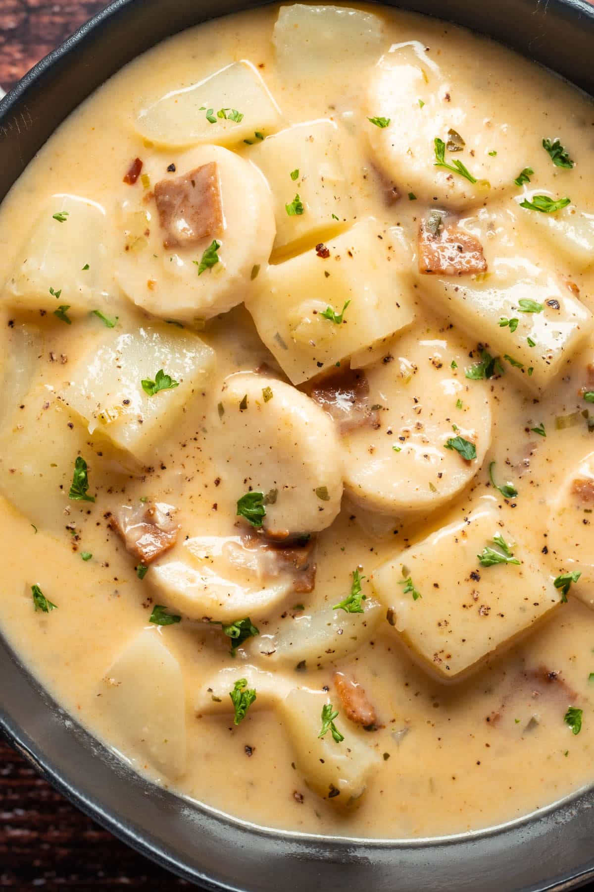 Vegan clam chowder topped with fresh chopped parsley in a black bowl.