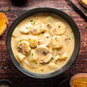 Vegan clam chowder with chopped parsley in a black bowl.