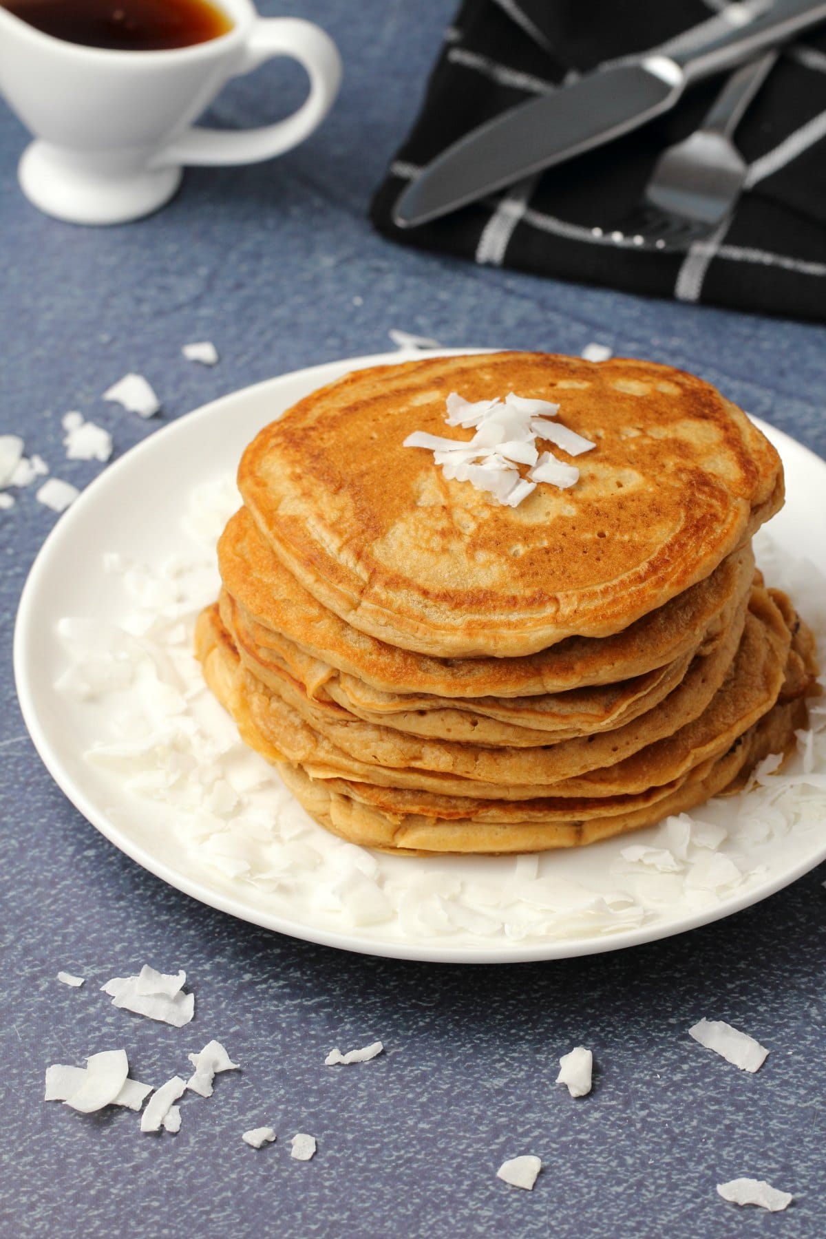 Vegan coconut pancakes topped with coconut flakes and stacked up on a white plate. 