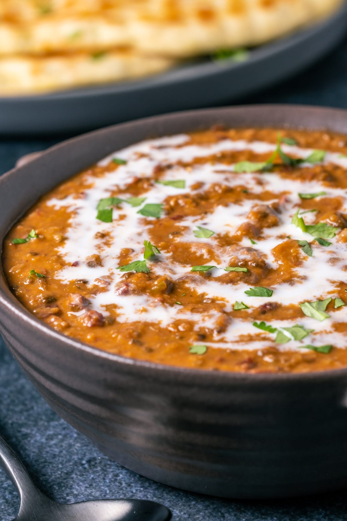 Vegan dal makhani topped with a drizzle of coconut cream and fresh chopped cilantro in a brown bowl.