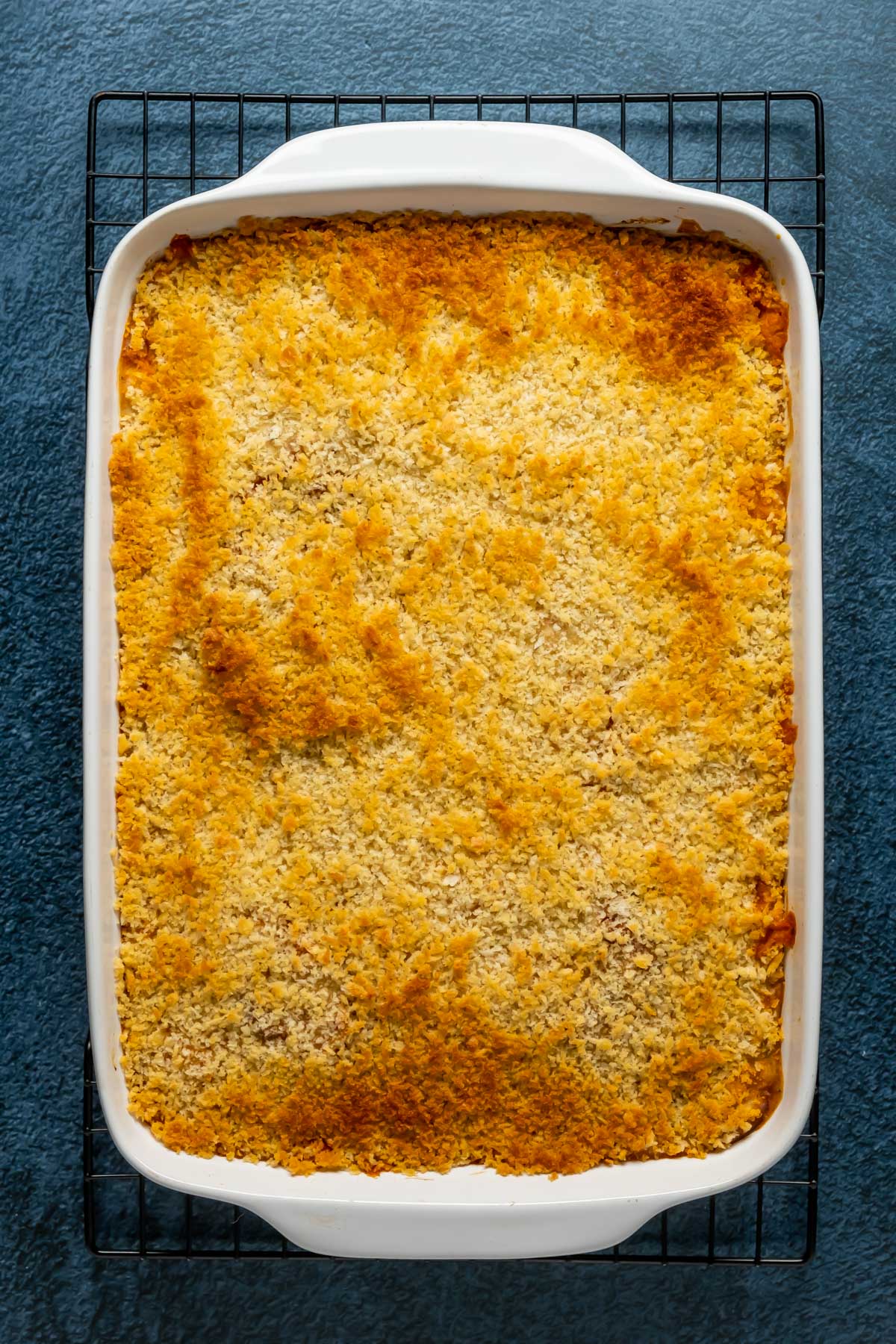 Freshly baked vegan eggplant parmesan in a white dish cooling on a wire cooling rack.