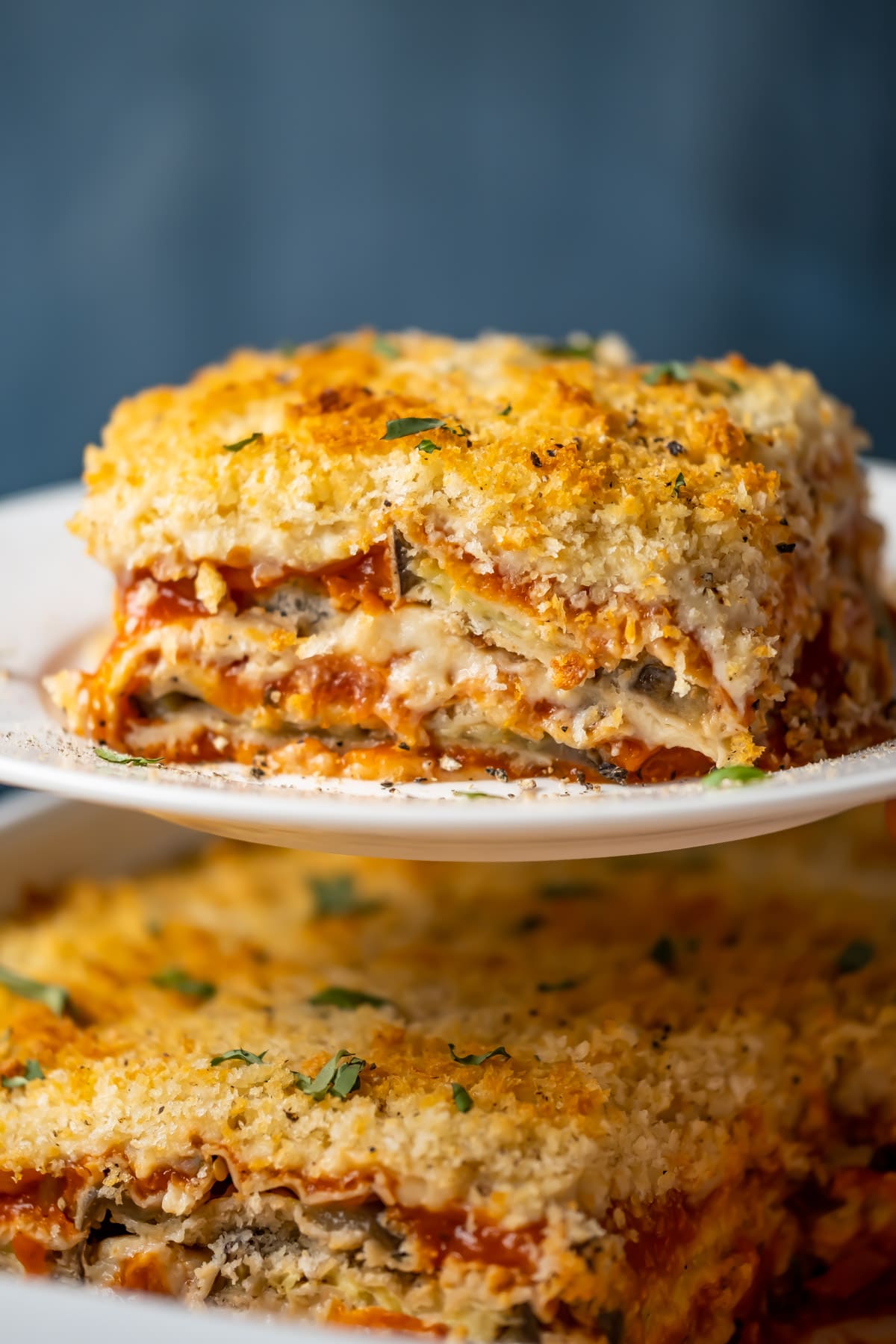 Slice of vegan eggplant parmesan on a white plate. 