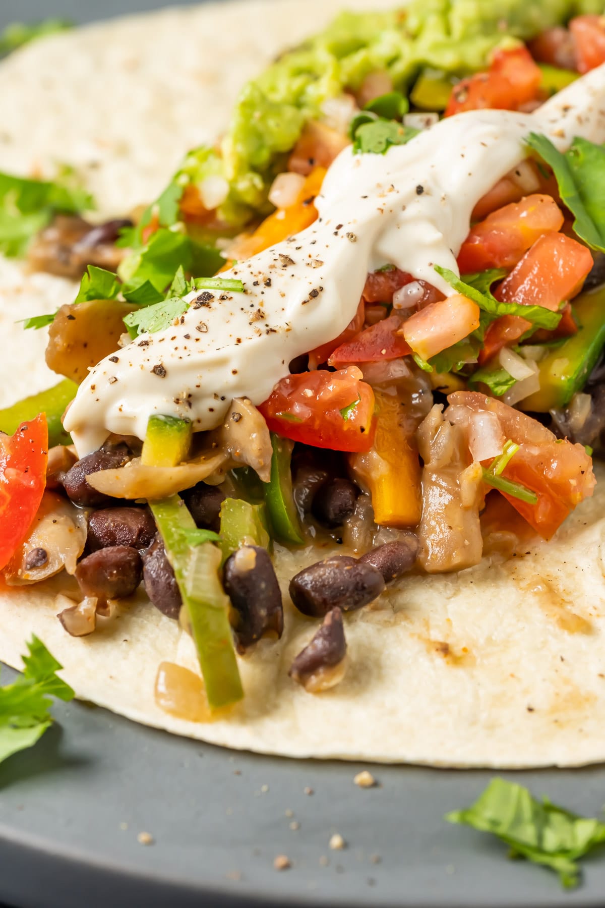 An open faced vegan fajita with sautéed veggies, pico de gallo, guacamole and vegan sour cream in a tortilla.