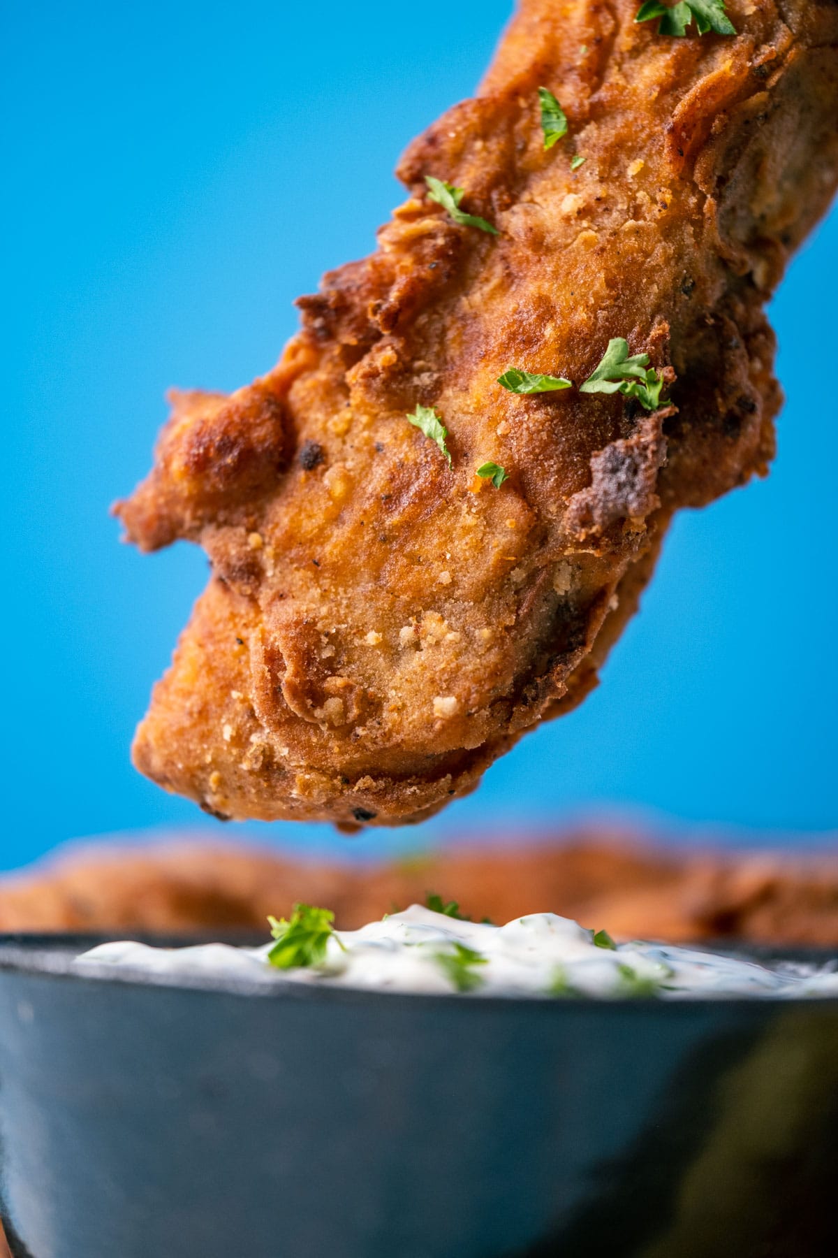 Vegan fried chicken piece about to dip into a bowl of vegan ranch dressing.