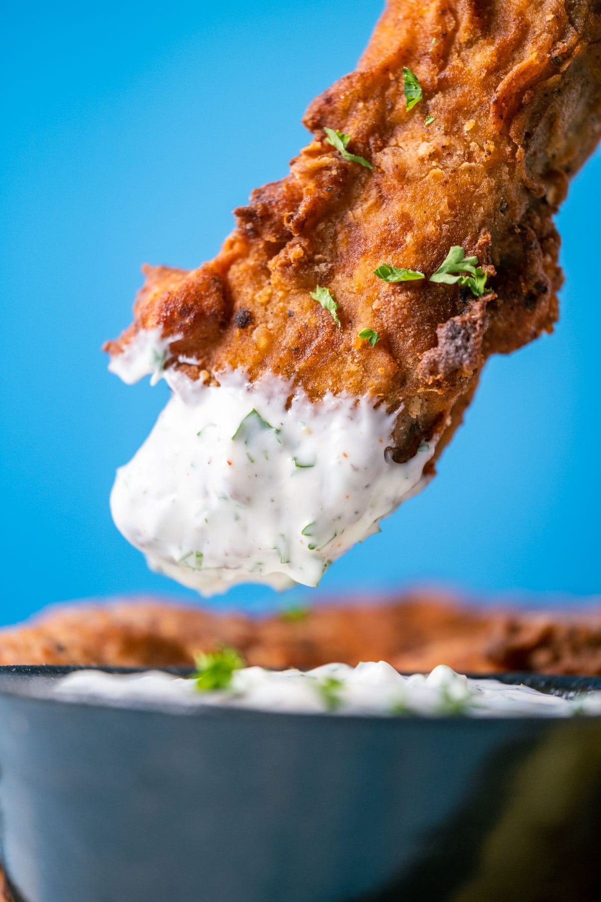 Piece of vegan fried chicken dipped in vegan ranch dressing.