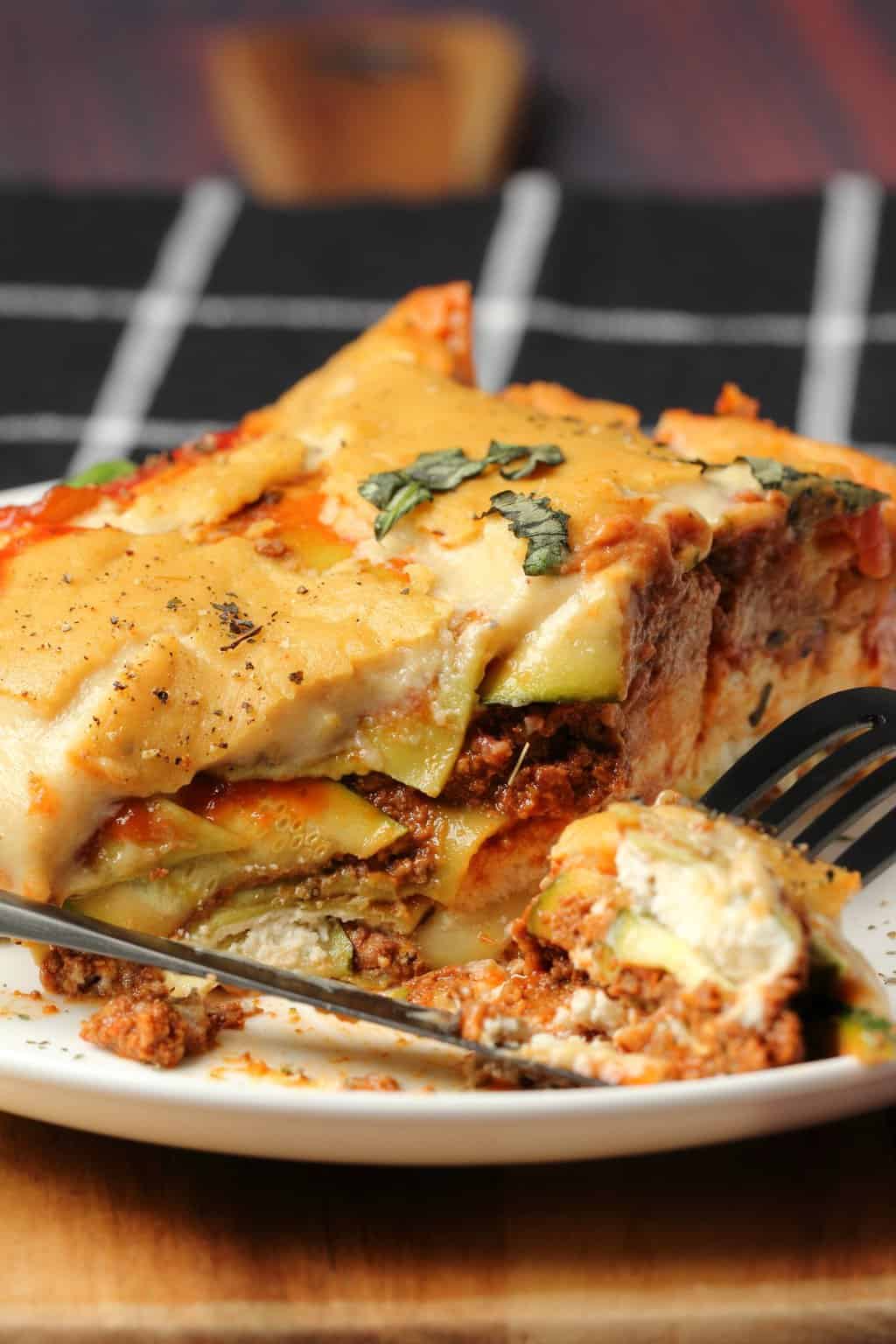 Slice of vegan lasagna on a white plate with a fork. 