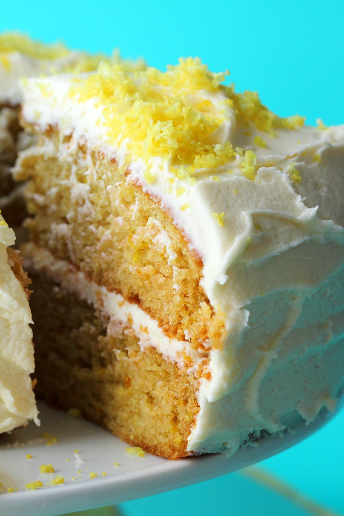 Lemon cake on a white cake stand with one slice cut and ready to be served. 