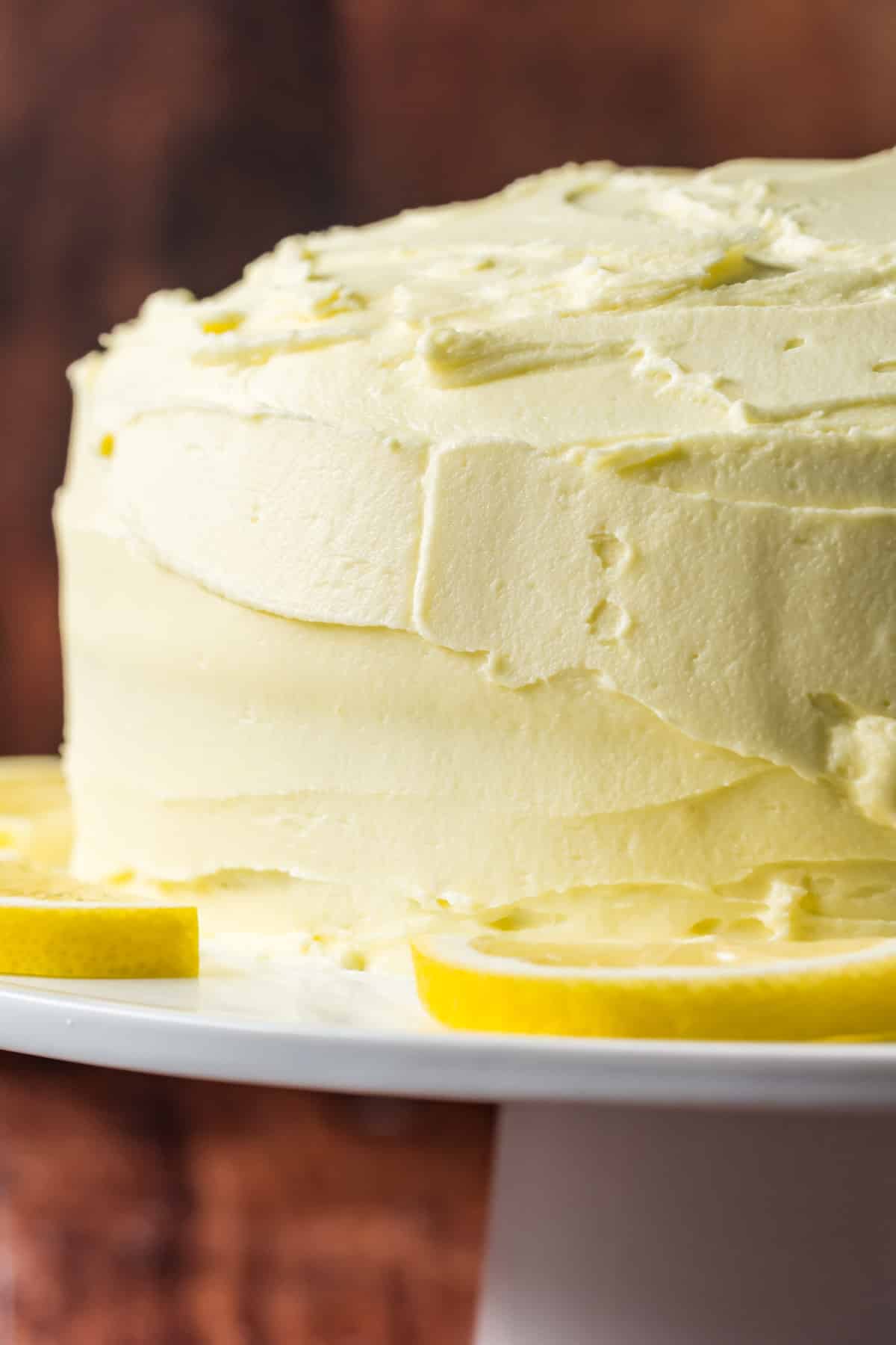 Frosted vegan lemon poppy seed cake on white cake stand.