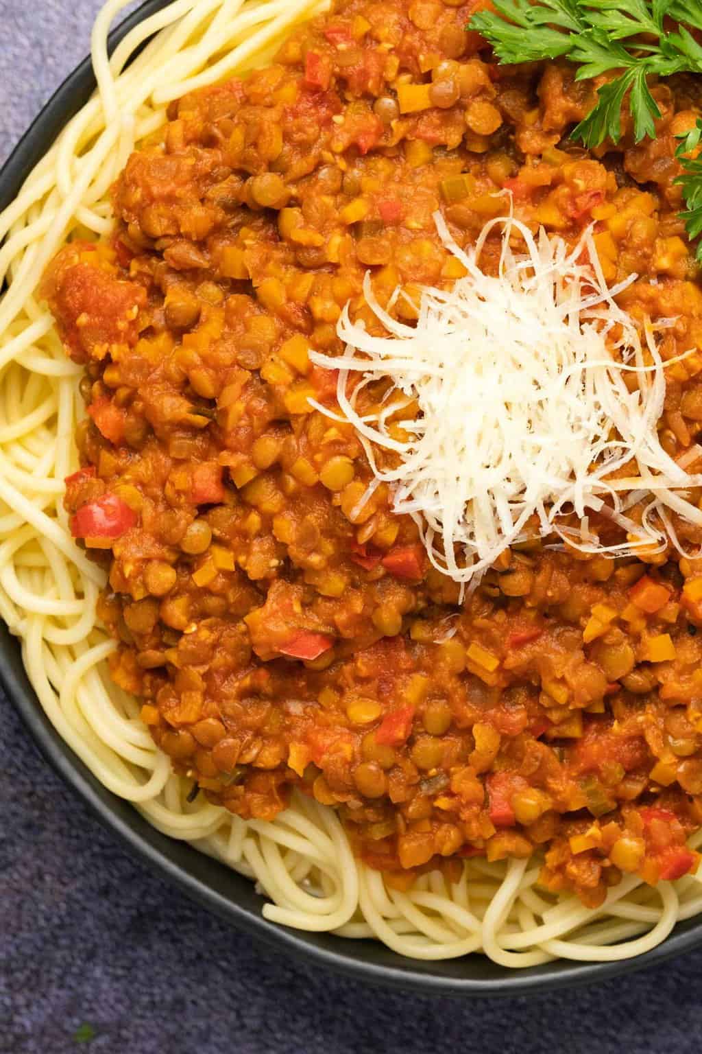 Lentil bolognese topped with vegan parmesan and parsley in a black bowl. 