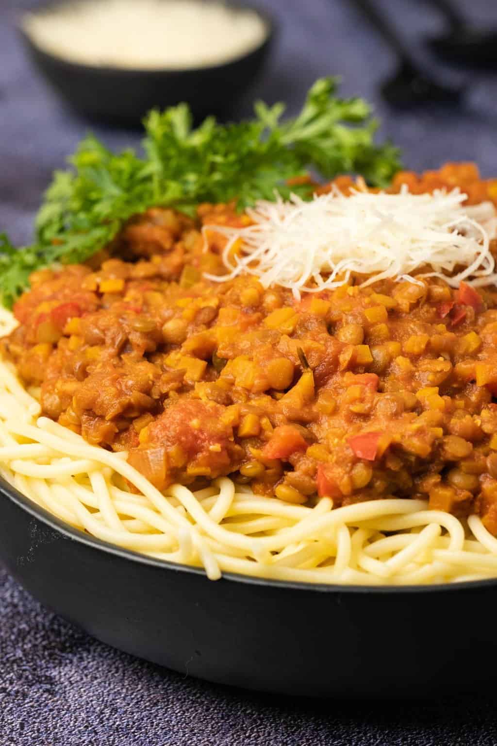 Lentil bolognese with spaghetti and vegan parmesan in a black bowl.