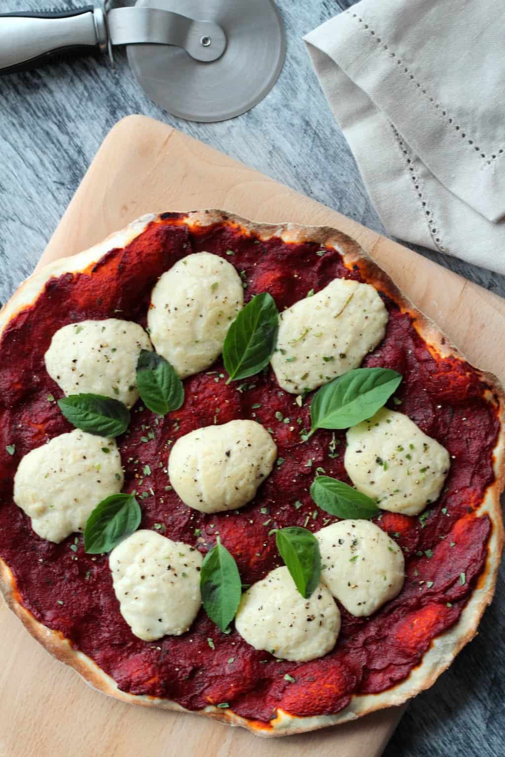 Vegan Mozzarella balls nicely melted on top of a pizza fresh from the oven, with basil leaves and dried herbs on top. 