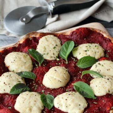 Vegan mozzarella on a pizza with fresh basil leaves.