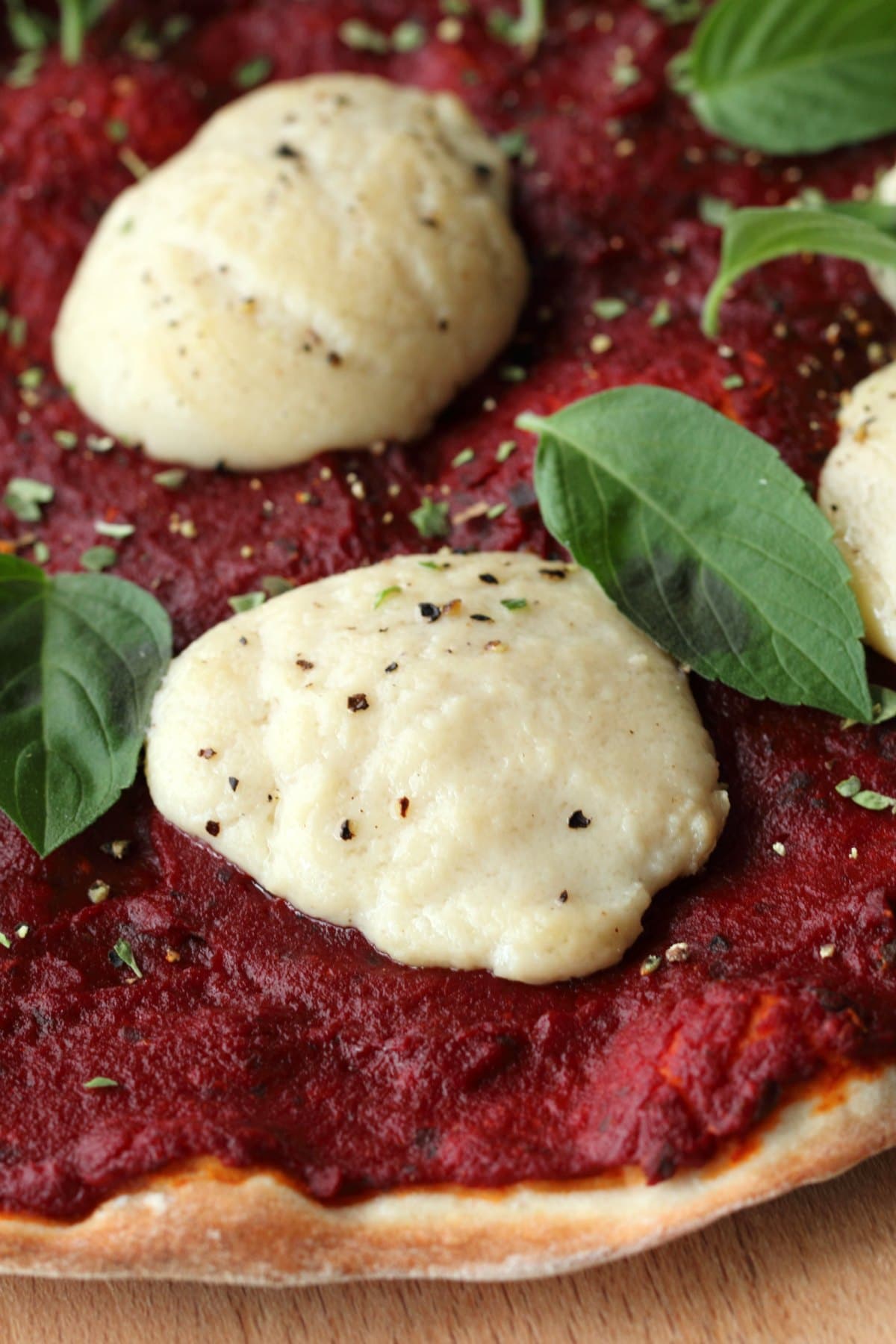 Vegan Mozzarella balls melted on top of a pizza, fresh basil leaves and dried herbs on top. 