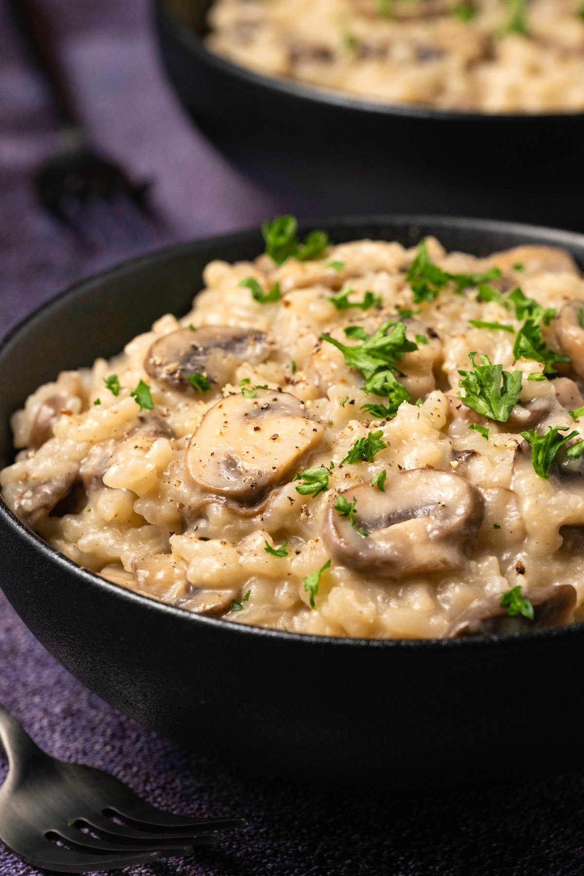 Vegan mushroom risotto in a black bowl. 